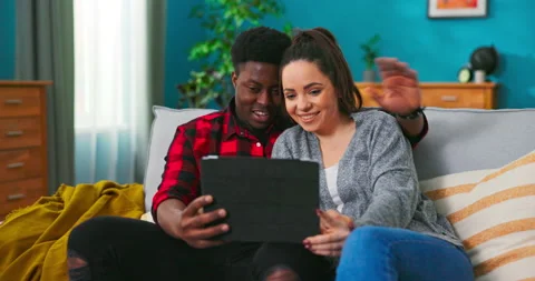 Multi-ethnic American nice young couple sitting on the grey couch in the cozy Stockbeeldmateriaal 152351773