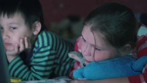 Multi-ethnic boy and white girl lying on the couch watching the notebook in the Stock Footage 77284013