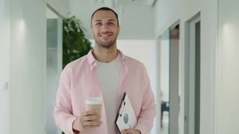Multi Ethnic Business Guy Walking in Corridor in Workspace Holding Coffee and Stock-Footage 247265317