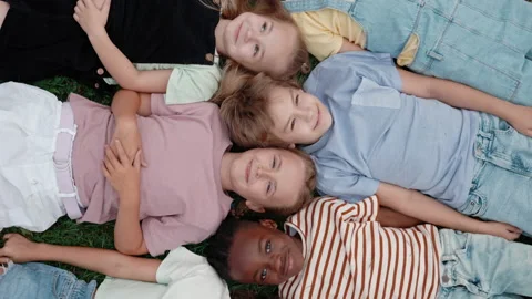Multi ethnic children lying head to head on schoolyard Stock Footage