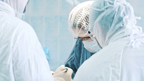 Multi-ethnic cooperating team of doctors and surgeons processing surgical Stock Footage 229876417