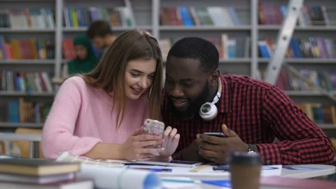 Multi ethnic couple browsing cellphone in library Stock Footage 101998237