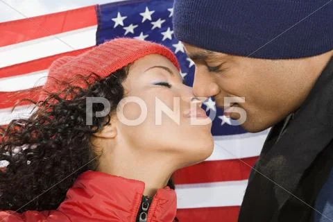 Multi-ethnic couple kissing in front of American flag Stock Photos