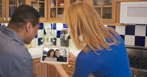 Multi Ethnic couple in kitchen video chatting with daughter and her boyfriend Stock Footage 117946235