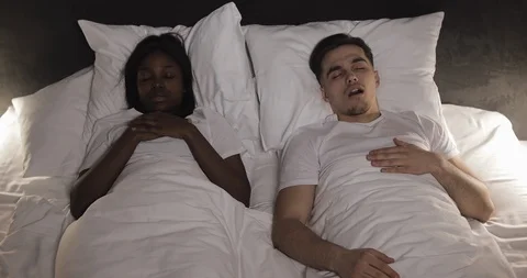 Multi-ethnic couple lying in bed together. Woman suffers from her partner Stock Footage 108115149