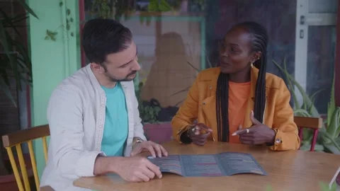 Multi-ethnic couple reading restaurant menu and picking dishes to order Stock Footage 244546225