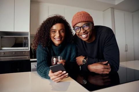 Multi-ethnic couple smiling at camera while in kitchen in modern apartment using Stock Photos