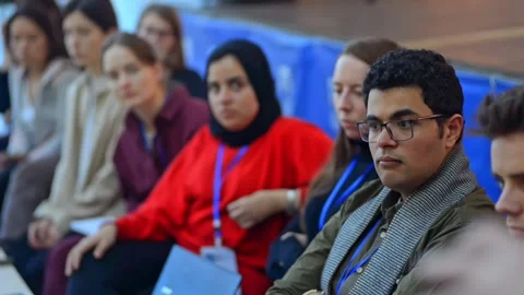 Multi ethnic diverse seminar audience sit on chairs and listen to leader on Stock Footage 137560198