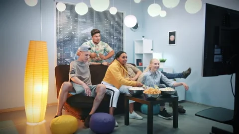 Multi-ethnic friends falling down on sofa to watch TV Stock Footage 151958333