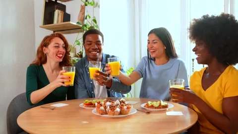 Multi-ethnic friends toasting over breakfast with orange juice and muffins .. Stock Footage 235906818