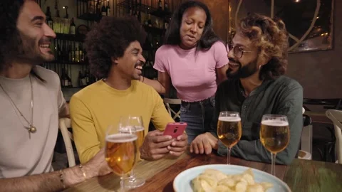 Multi-ethnic group friends looking smiling social networks on cell phone in pub Stock Footage 234112665