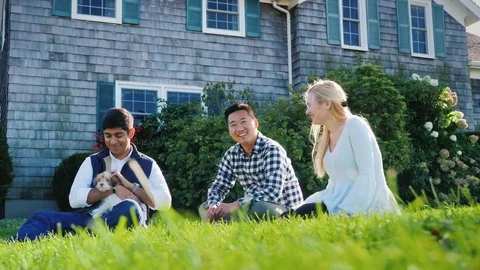 A multi-ethnic group of friends is resting in the backyard, sitting on the lawn Stock Footage 83049491