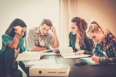 Multi ethnic group of students preparing for exams in home interior behind ta Stock Photos