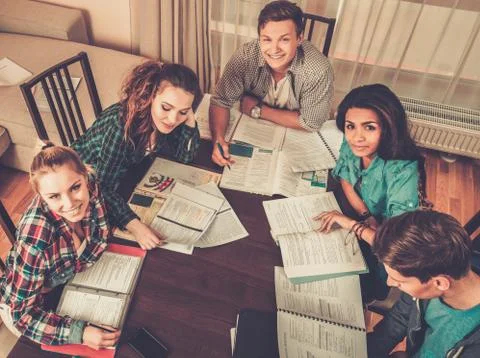 Multi ethnic group of students preparing for exams in home interior behind ta Stock Photos