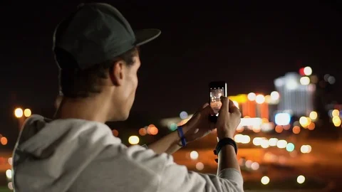 Multi-ethnic guy takes some photos of night city on his smartphone, close-up Stock Footage 115743211