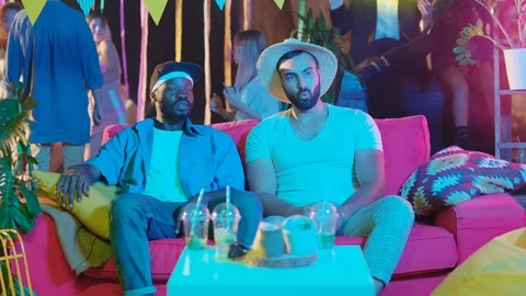 Multi-ethnic handsome friends sitting on red coach looking at girls passing by Stock Footage 115357367