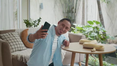 Multi-ethnic Man Taking Selfies on Mobile Phone with Albino Snake at Home Stock Footage 304540067