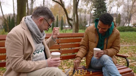 Multi-ethnic men playing chess in autumn park on a bench. Stock Footage 271325606