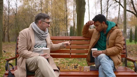 Multi-ethnic men playing chess in autumn park on a bench. Stock Footage 271325608