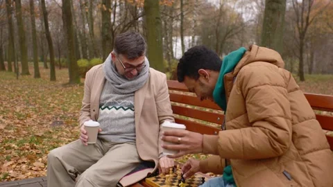 Multi-ethnic men playing chess in autumn park on a bench. Stock Footage 271325614
