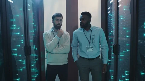 Multi-ethnic server technicians walking along rack server corridor in computer Stock Footage 119081319