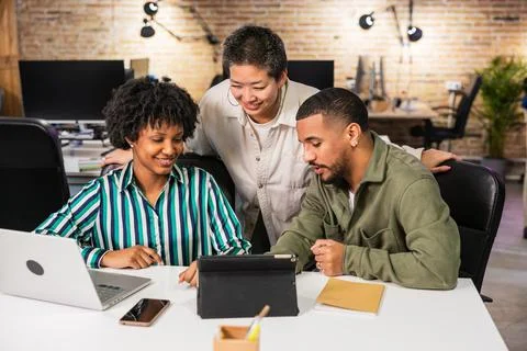 Multi ethnic team collaborating on project using tablet in modern office Stock Photos