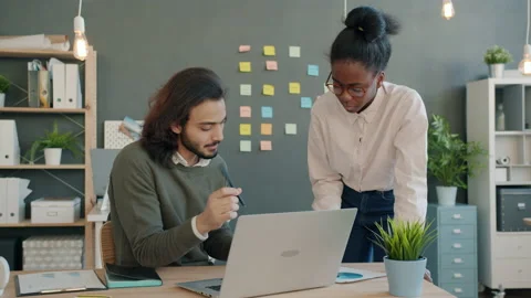 Multi-ethnic team girl and guy talking and looking at papers and laptop screen Stock Footage