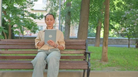 Multi Ethnic Woman Using a Digital Tablet on a Park Bench Stockbeeldmateriaal 310594284