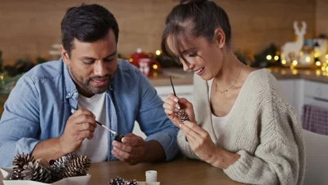 Multi ethnicity couple decorating cone with white paint during Christmas time at Stock Footage 218782541