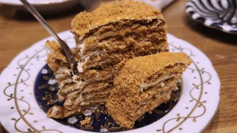 A multi-layered sweet cake in a plate on the table is eaten with a spoon. Stock Footage 221150852