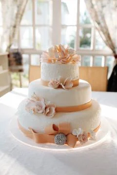 A multi level white wedding cake on white table and pink flowers on top Stock-Fotos