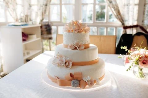 A multi level white wedding cake on white table and pink flowers on top Stock Photos