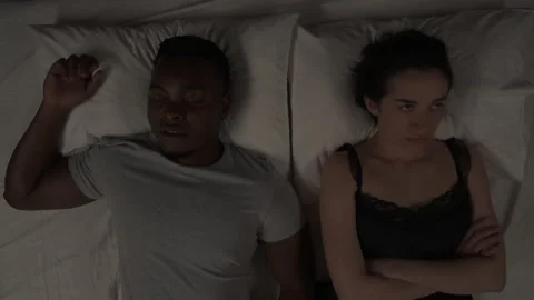 Multi-raced couple lying in bed at night. Annoyed Caucasian girl covering her Stock Footage 136575108