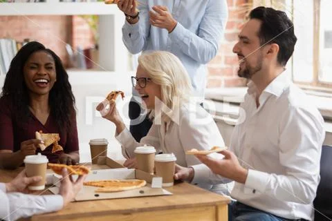 Multi racial colleagues eat pizza enjoy break during working day Stock Photos