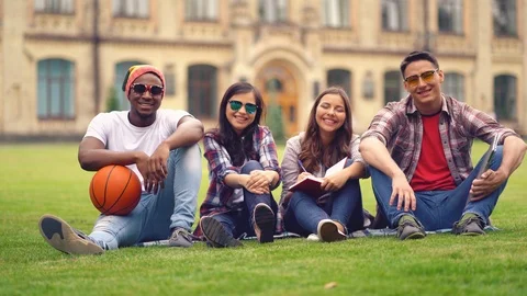 Multi racial students sit on a green grass with basketball ball Stock Footage 126719593