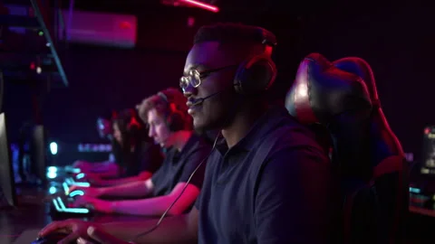 Multi-racial teammates sit in their gaming seats, put on headsets and Stock Footage 152346579