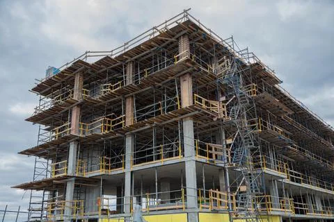 Multi-story building under construction with scaffolding against cloudy sky 库存照片