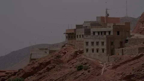 Multi-story concrete and earthen buildings cling to the jagged red rocky Vídeos de archivo 346106582