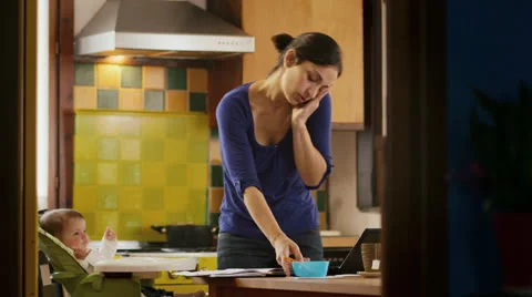 Multi-tasking mom cooking and working, feeding child in home kitchen Stock Footage 24310528