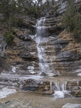 Multi-tier waterfall cascading over rocky cliffs surrounded by evergreens and 库存照片