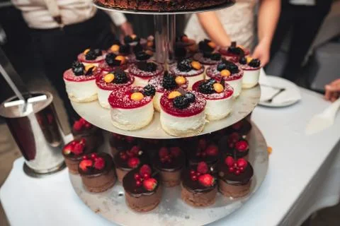 Multi-tiered plate stand with small sweet cakes decorated with fresh fruit Stock Photos