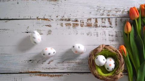 Multicolor Easter eggs rolling on white wooden table with tulips.  Stock Footage 150380293