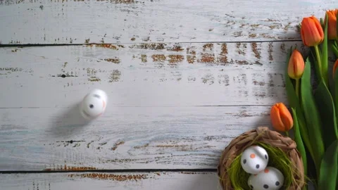Multicolor Easter eggs rolling on white wooden table with tulips.  Stock Footage 150380333