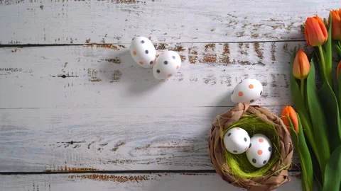 Multicolor Easter eggs rolling on white wooden table with tulips.  Stock Footage 150380423