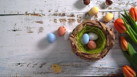 Multicolor Easter eggs rolling on white wooden table with tulips.  Stock Footage 150380709