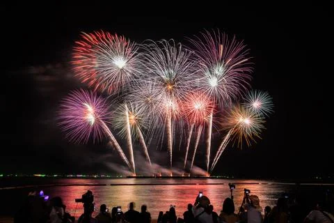 Multicolor Fireworks Display Exploding Over Tranquil Bay With Spectators Wi.. Foto stock