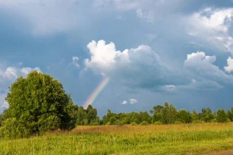 Multicolor rainbow on the background of a beautiful cloudy sky and a small fi Stock Photos