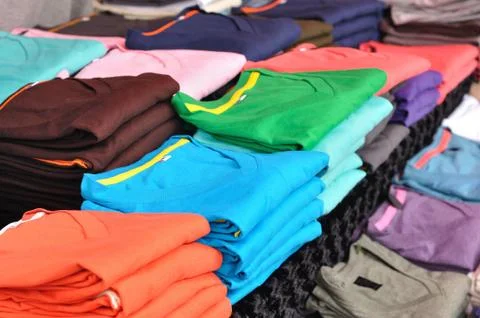 Multicolor t-shirts stacking on table in market fair. Stock Photos