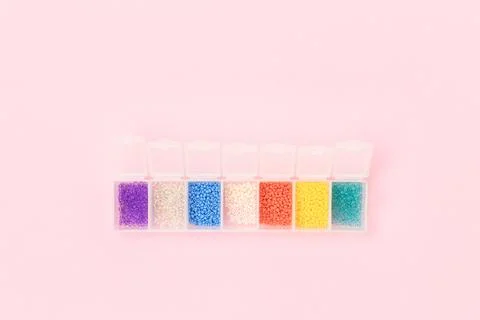 Multicolored beads in a storage container on a pink pastel background. Stock Photos