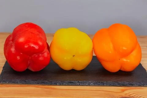 Multicolored bell peppers on flat slate serving plate, front view Stock Photos